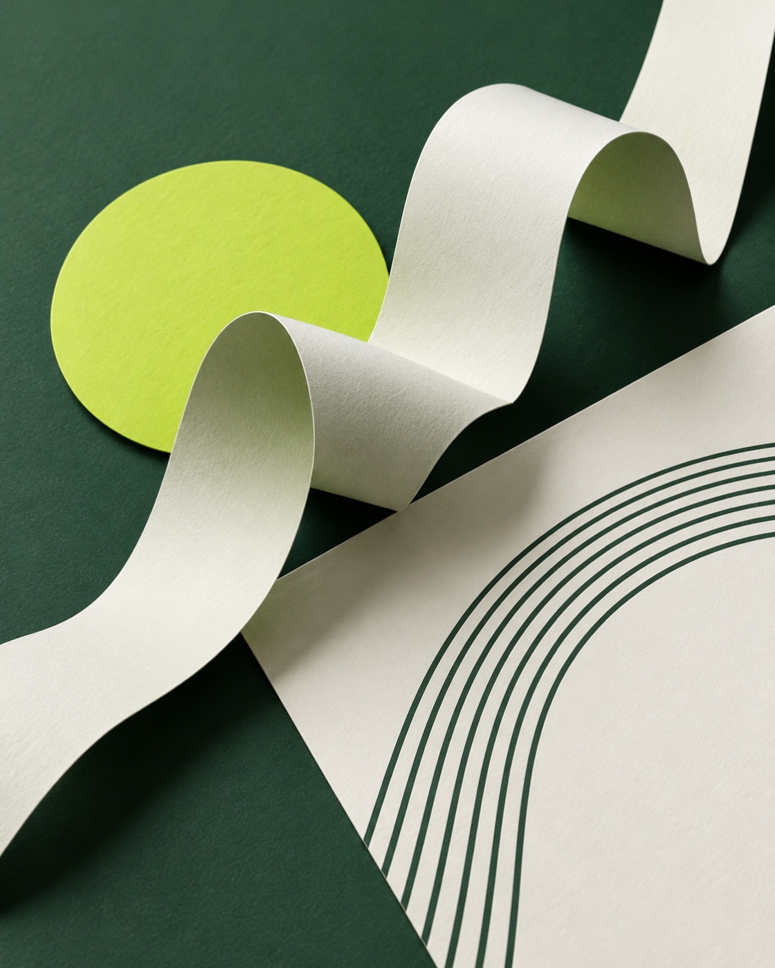 Sculptural green paper ribbons, a lime circle and folded ivory paper in a sunlit design studio.